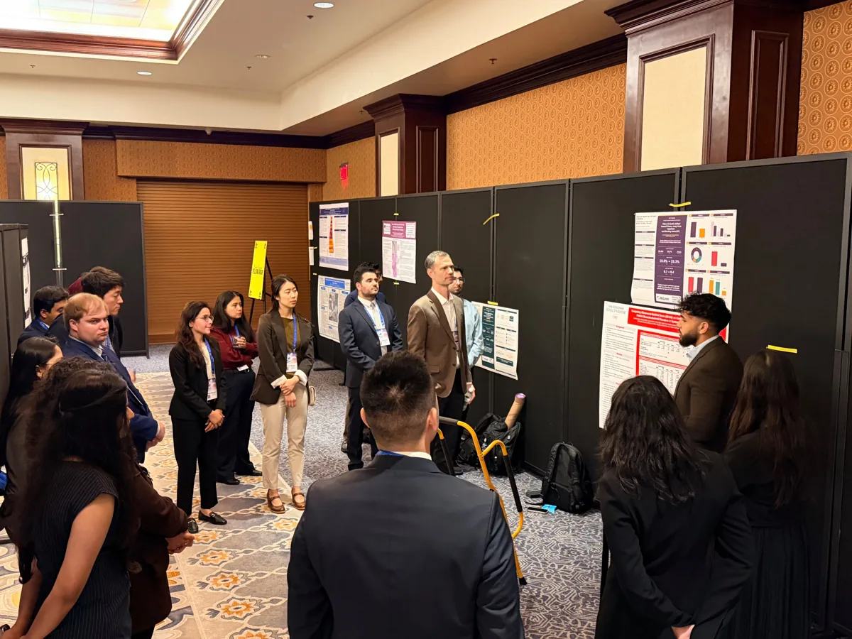A group discussing findings beside a red and white research poster.