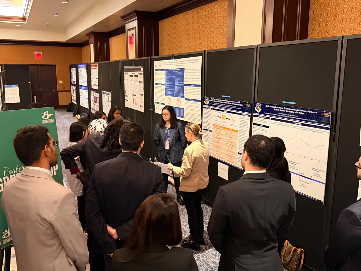 Attendees listening to an investigator beside a blue and white poster.